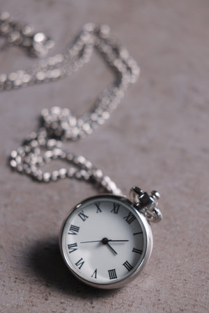 Silver pocket clock with chain on gray textured table, closeup