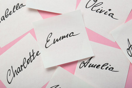 Paper stickers with different names on pink background, top view. Choosing baby's name
