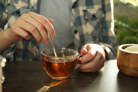 Woman stirring tea with spoon at dark table, closeupの写真素材