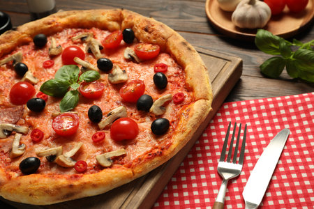 Delicious pizza with tomatoes, mushrooms, black olives and basil served on wooden table, closeupの写真素材