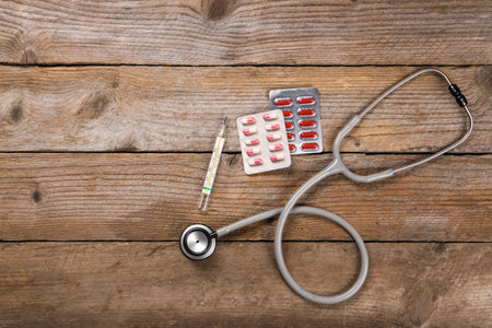 Stethoscope, thermometer and pills on wooden background, flat lay. Space for textの写真素材