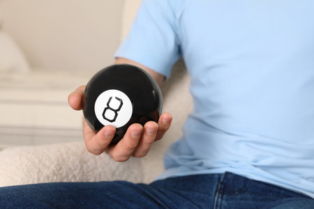 Man holding magic eight ball indoors, closeup