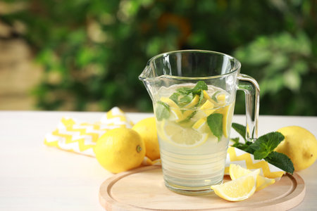 Refreshing lemonade with mint in jug on light table against blurred green background. Space for textの写真素材