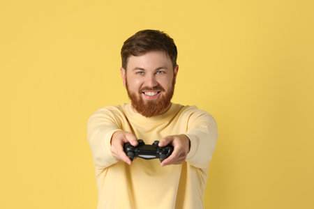 Happy man with game controller on pale yellow background