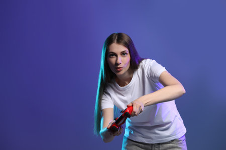 Surprised woman playing video games with controller on violet background, space for textの写真素材