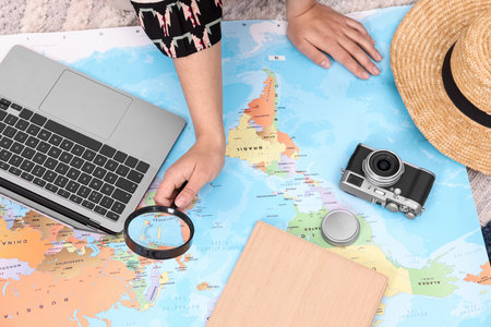 Travel blogger with magnifying glass and map planning trip, top view