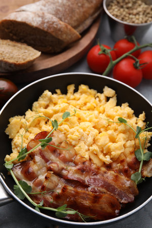 Delicious scrambled eggs with bacon in frying pan on gray tableの写真素材