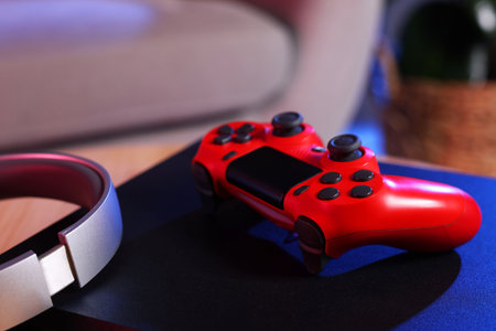 Video game console, wireless controller and headphones on table indoors, closeup