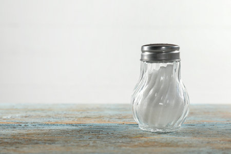 Salt shaker on light blue wooden table, closeup. Space for text