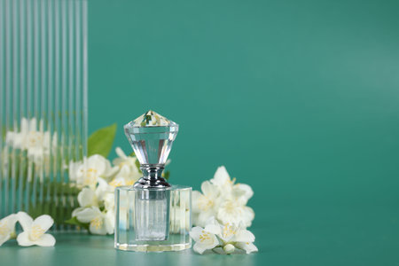 Aromatic perfume in bottle and beautiful jasmine flowers on green background, space for textの写真素材