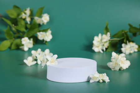 Presentation of product. White podium and beautiful jasmine flowers on green background