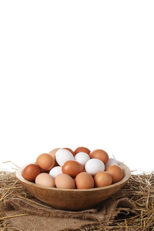 Fresh chicken eggs in bowl and dried straw on table against white backgroundの写真素材