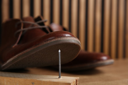 Metal nails in wooden plank and shoes on table, closeup