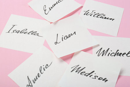 Paper stickers with different names on pink background, closeup. Choosing baby's name