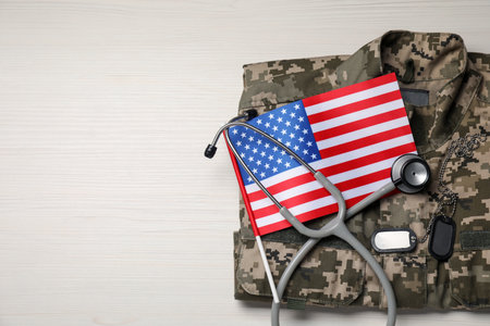 Stethoscope, USA flag, tags and military uniform on white wooden table, top view. Space for text