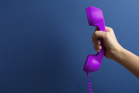 Woman holding purple telephone handset on blue background, closeup. Space for textの写真素材