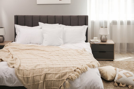 Many soft white pillows and knitted blanket on bed indoors