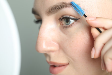 Young woman with spoolie brush on light background, closeup. Eyebrow correction