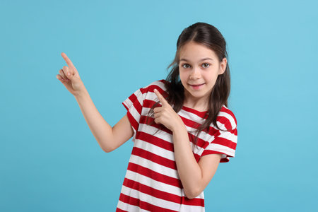 Portrait of beautiful girl pointing at something on light blue backgroundの写真素材