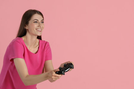 Happy woman playing video games with controller on pink background, space for textの写真素材