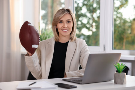 Smiling woman with american football ball at table in officeの写真素材