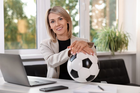 Smiling woman with soccer ball at table in office