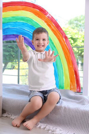 Little boy near rainbow painting on window indoorsの写真素材