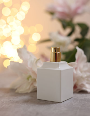 Bottle of perfume and beautiful lily flowers on table against beige background with blurred lights,...