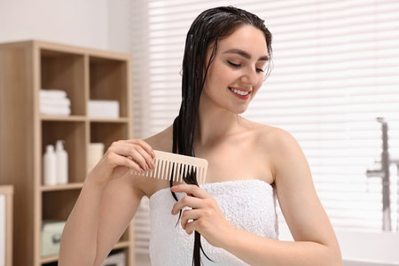 Smiling woman combing her hair with applied mask in bathroomの写真素材