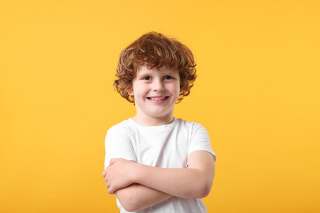 Portrait of cute little boy with crossed arms on orange backgroundの写真素材