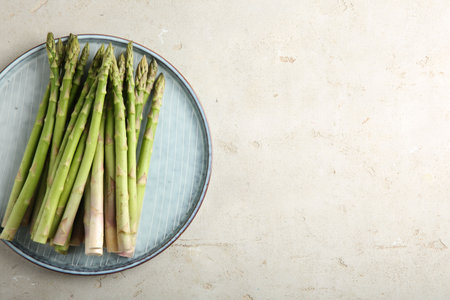 Plate with fresh green asparagus stems on light textured table, top view. Space for textの写真素材