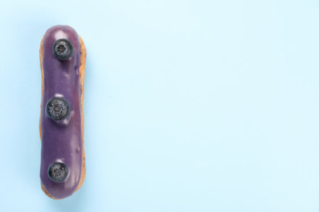 Delicious eclair covered with glaze on light blue background, top view. Space for text