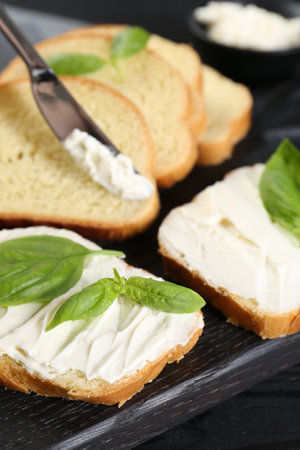 Pieces of bread with cream cheese and basil leaves on black table, closeupの写真素材