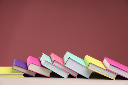 Many colorful books on beige table against pink background, space for textの写真素材
