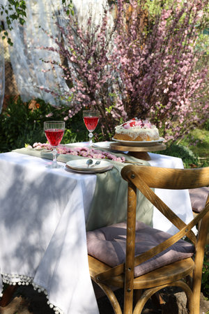Beautiful spring flowers, delicious cake and wine glasses on table in gardenの写真素材