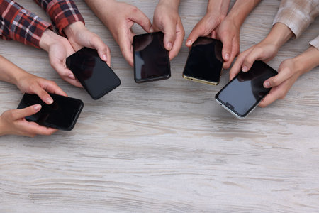 People holding smartphones with blank screens at wooden table, top view. Mockup for designの写真素材