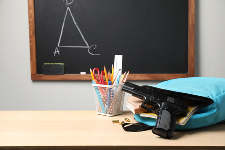 Gun, bullets and school stationery on wooden table near blackboard indoors, space for textの写真素材