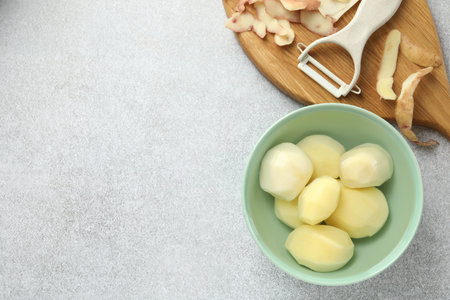 Fresh raw potatoes in bowl, peeler and peels on light grey table, top view. Space for textの写真素材