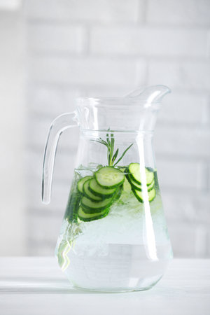 Refreshing cucumber water with rosemary in jug on white table against brick wallの写真素材