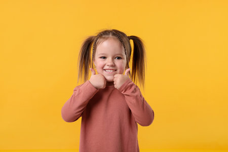 Cute little girl showing thumbs up on orange background