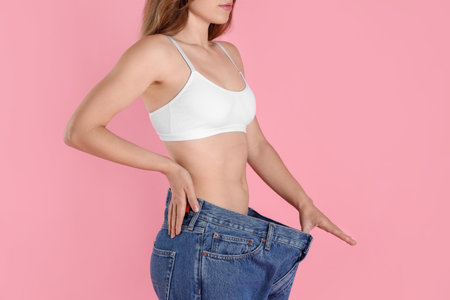 Woman in big jeans showing her slim body on pink background, closeupの写真素材