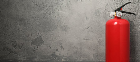 Fire extinguisher on grey textured background, space for text