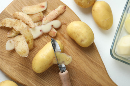 Fresh raw potatoes, peels and peeler on white table, top viewの写真素材
