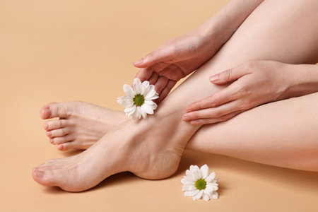 Closeup view of woman`s groomed feet after care procedure and beautiful flowers on beige backgroundの写真素材
