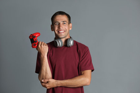 Happy man in headphones with controller on gray background