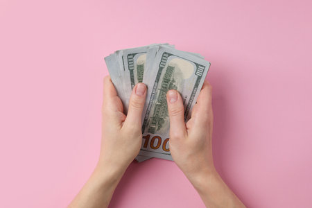 Money exchange. Woman holding dollar banknotes on pink background, top view