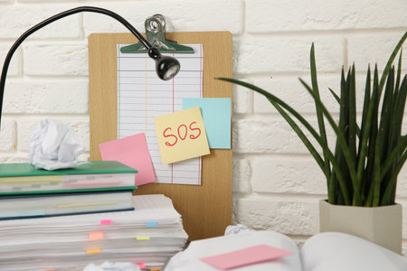 Note with word SOS and stationery on table at workplace