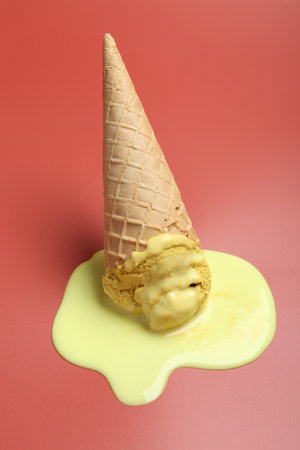 Melted ice cream in wafer cone on pale pink backgroundの写真素材