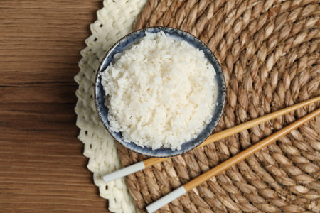 Tasty cooked rice in bowl and chopsticks on wooden table, flat layの写真素材