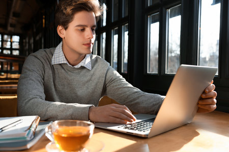 Teenage student with laptop studying at table in cafeの写真素材